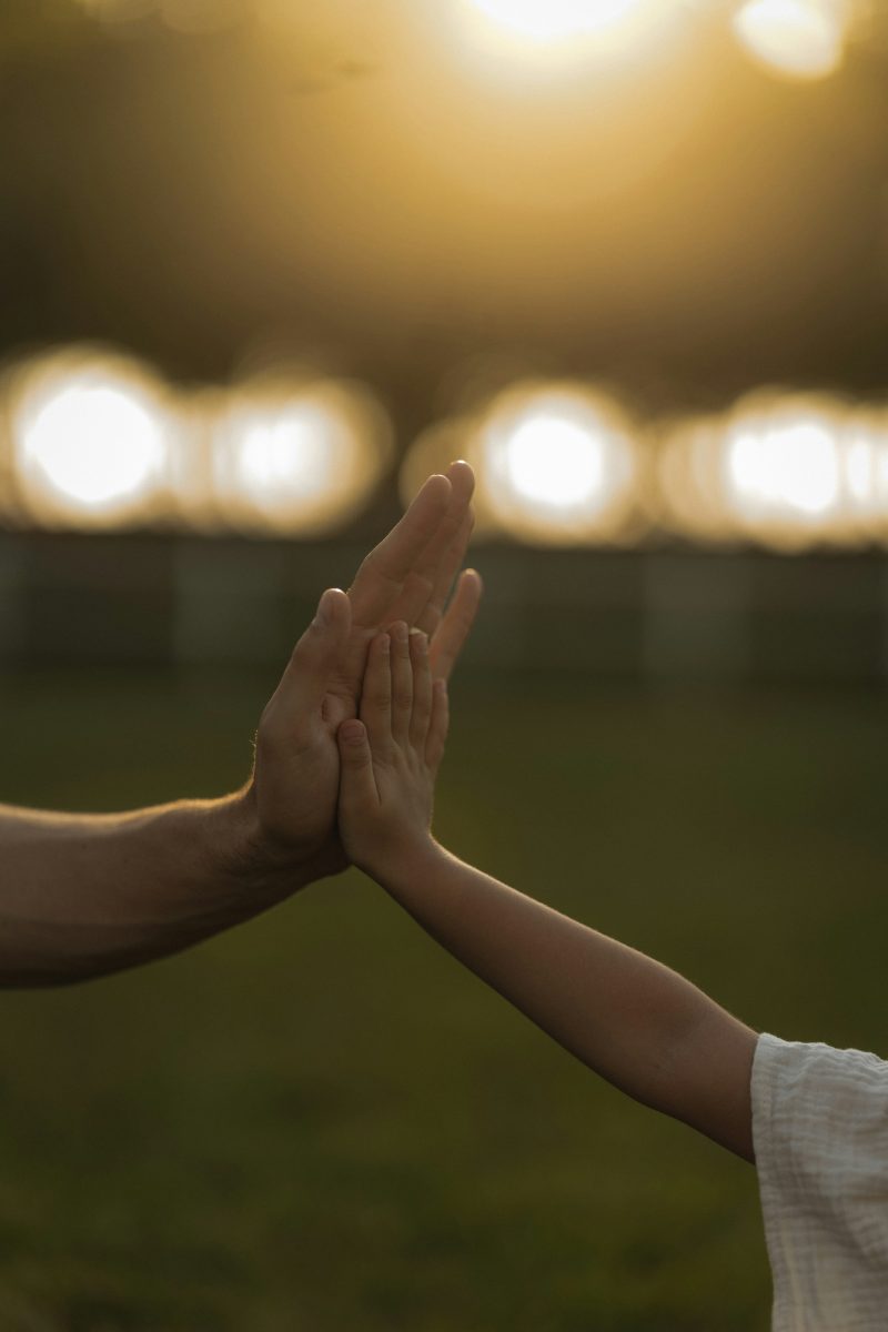 Die Hand eines Erwachsenen und eine Kinderhand klatschen im Gegenlicht ab