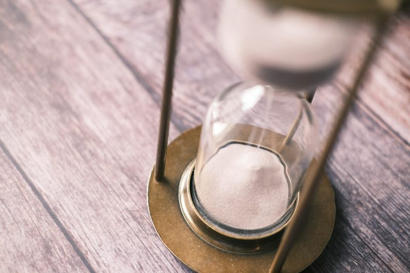 Eine Sanduhr mit Messingrahmen steht auf einem Holztisch, der Sand rieselt nach unten