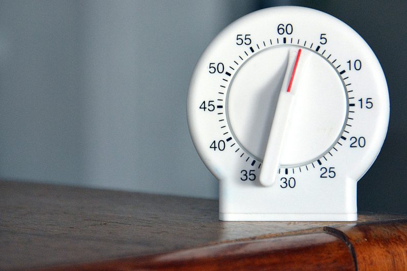 A kitchen timer next to an open exercise book and a pencil on a table