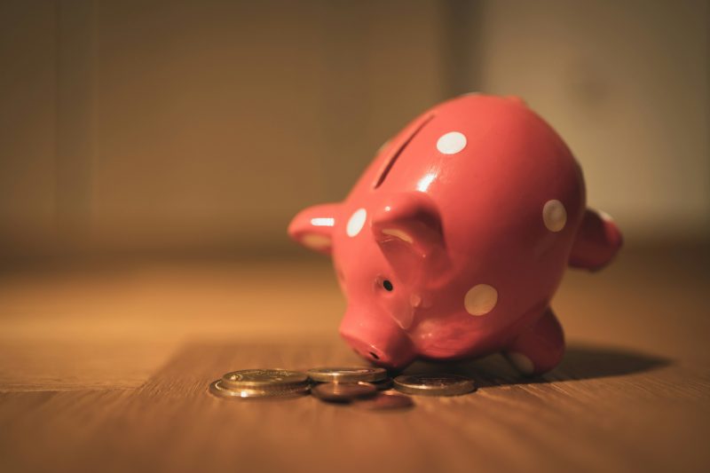 Ein rosa getupftes Sparschwein liegt auf einem Holztisch, darunter ein paar Münzen